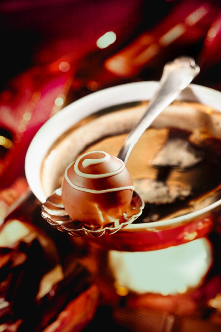 A praline on a spoon balanced over a coffee cup