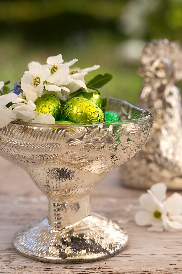 Silberne Schale gefüllt mit Schokoladeneier, Vergissmeinnicht Gartenjasmin und Schlehenblüten