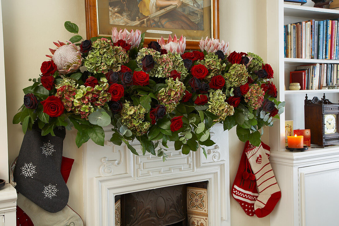 Üppige Girlande aus Rosen, Hortensien und Proteablüten als Weihnachtsschmuck auf dem Sims eines traditionellen, englischen Kamins
