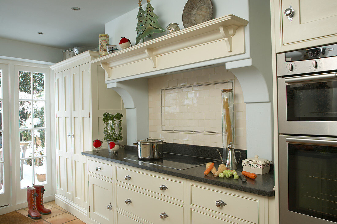 Cream country house kitchen in simple Shaker style with modern stainless steel appliances and masonry extractor hood