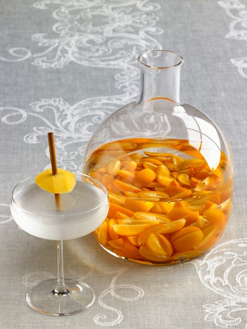 The Timber Cove Cocktail with Cinnamon Stick and Mango; Kumquat Nastoyka in a Glass Pitcher with Kumquats