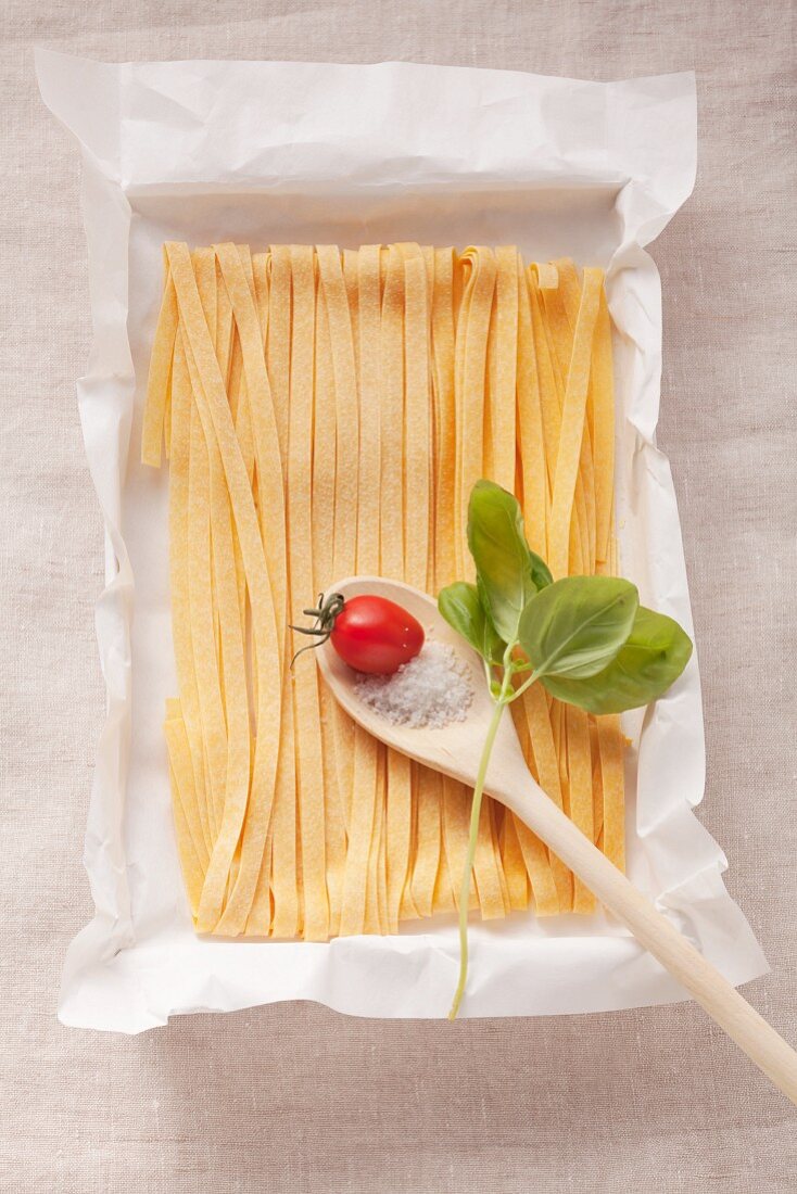 Tagliatelle and a tomato, salt and basil on a wooden spoon