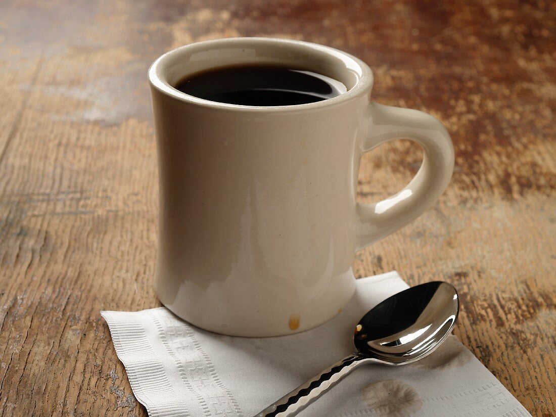 Tasse mit Kaffee auf Holzuntergrund mit Serviette und Löffel; Nahaufnahme
