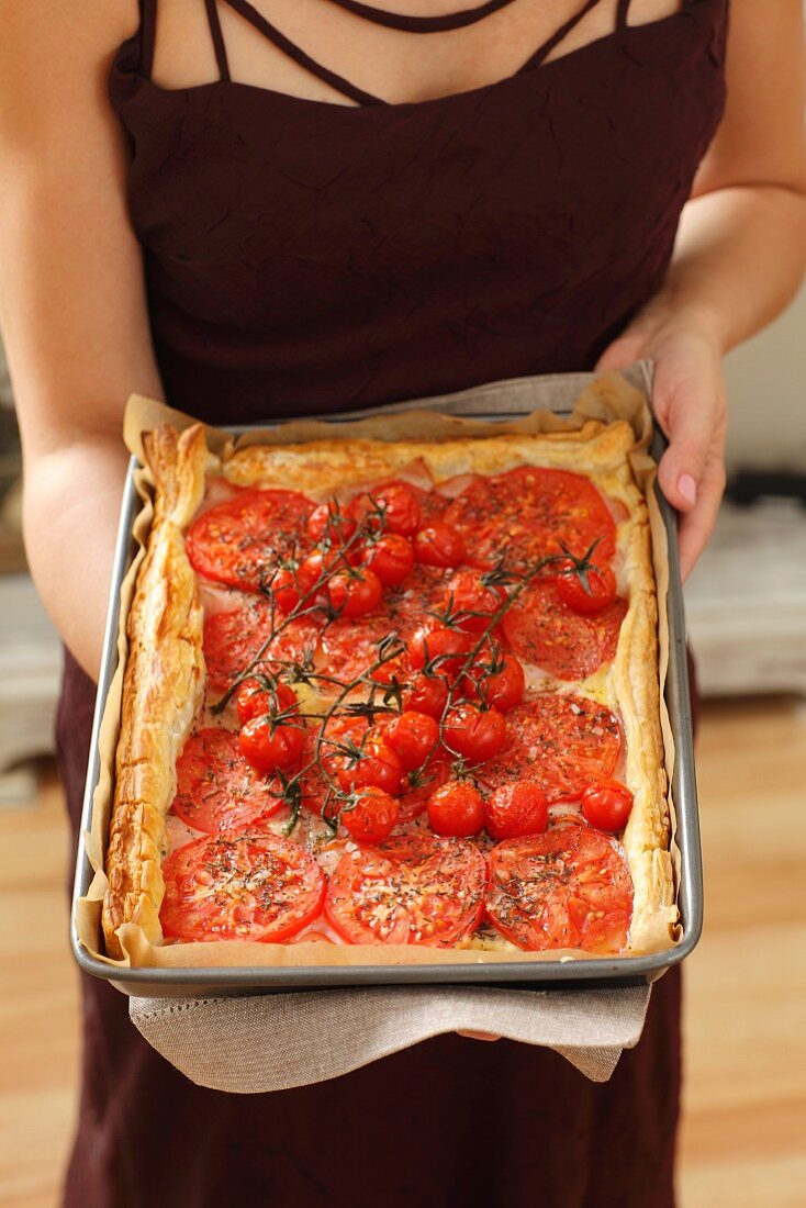 A woman holding a tomato, ham and cheese tart