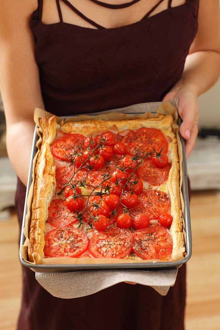 Frau hält Tomatentarte mit Schinken und Käse