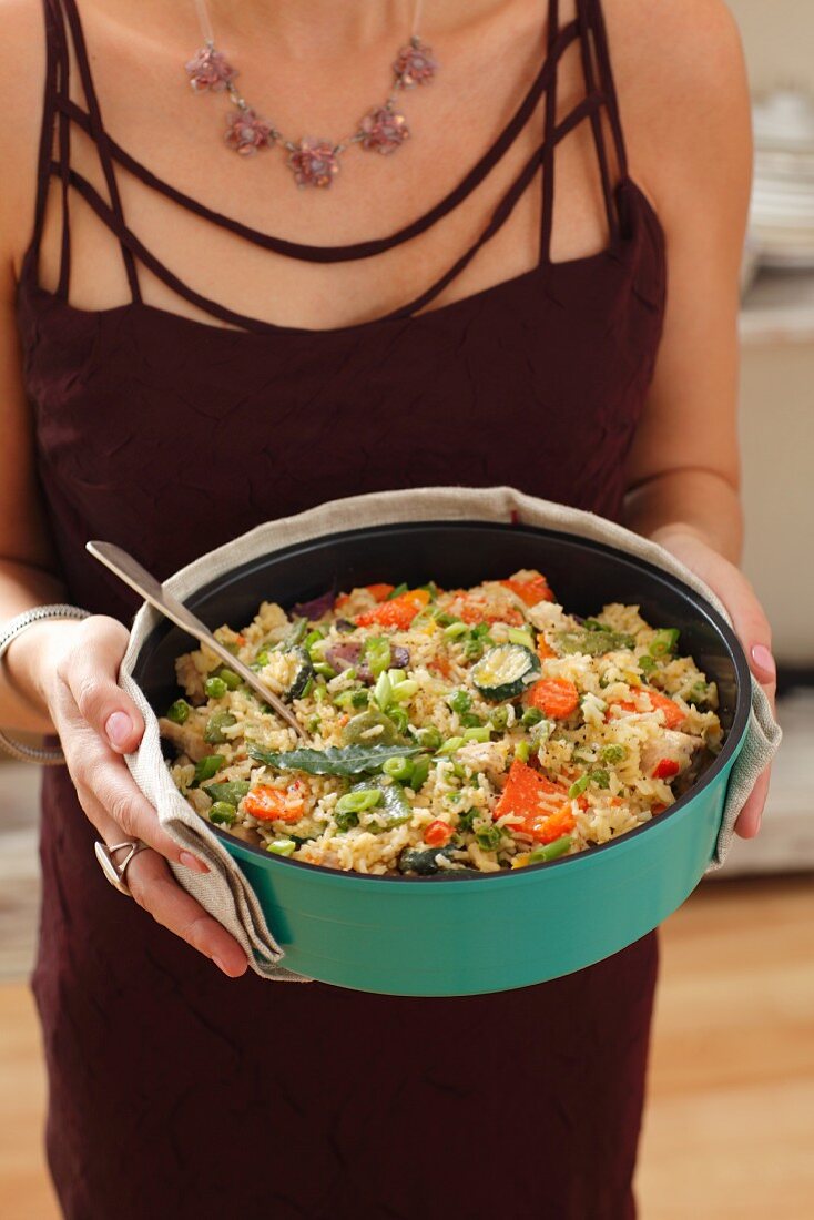 A woman holding a bowl of rice, turkey and vegetables