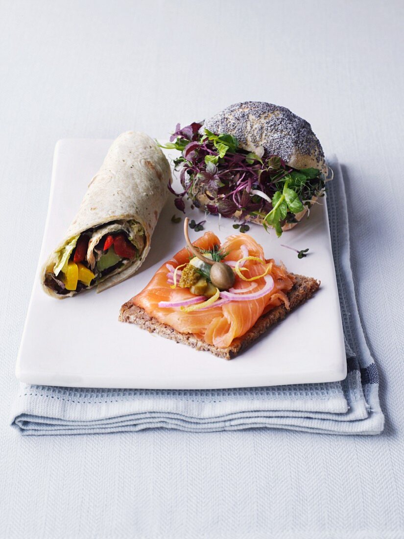 A wrap, a slice of wholemeal bread topped with salmon and a poppy seed roll filled with cress