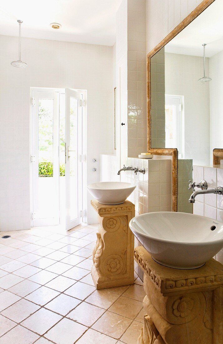 Two round sinks on free standing, Roman style pedestals in a light and bright bathroom with an entrance to a garden area