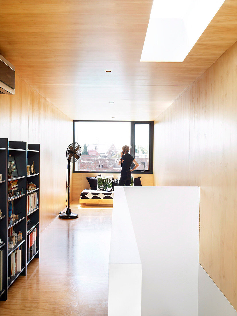 Half-height bookcase, sofa and standard fan in wood-clad room