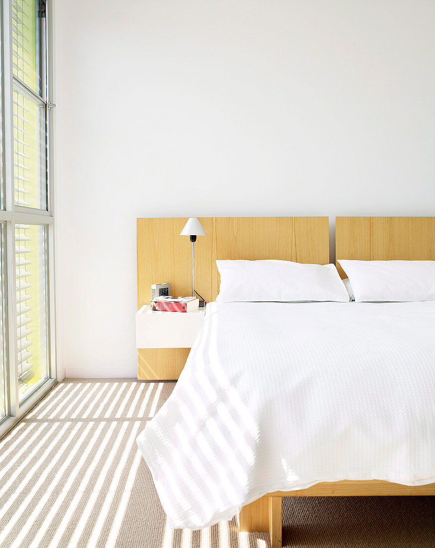 Sunlight shining through blinds into bedroom with double bed and white bed linen