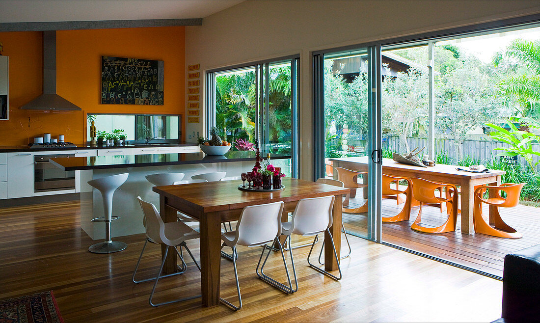 Blick aus dem offenen Wohnraum auf die großzügige Gartenterrasse mit modernen Kunststoffstühlen und einem langen Holztisch