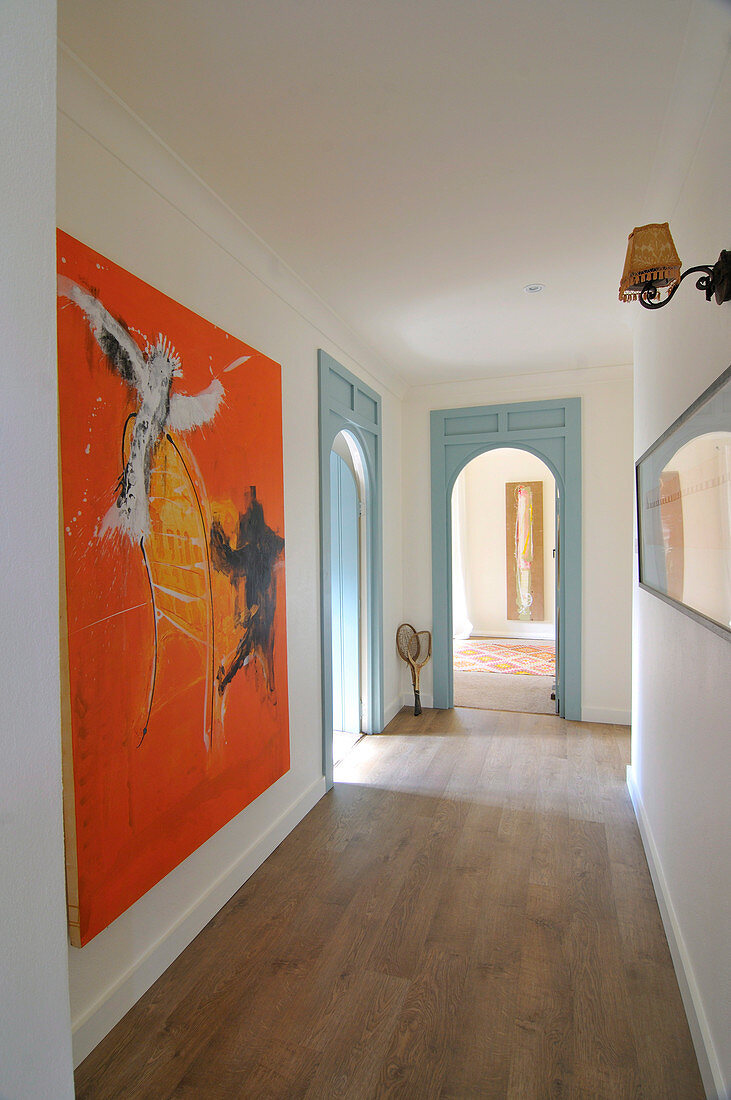 Langer Flur mit Holzboden, Rundbogen-Türöffnungen und Bildern an den Wänden