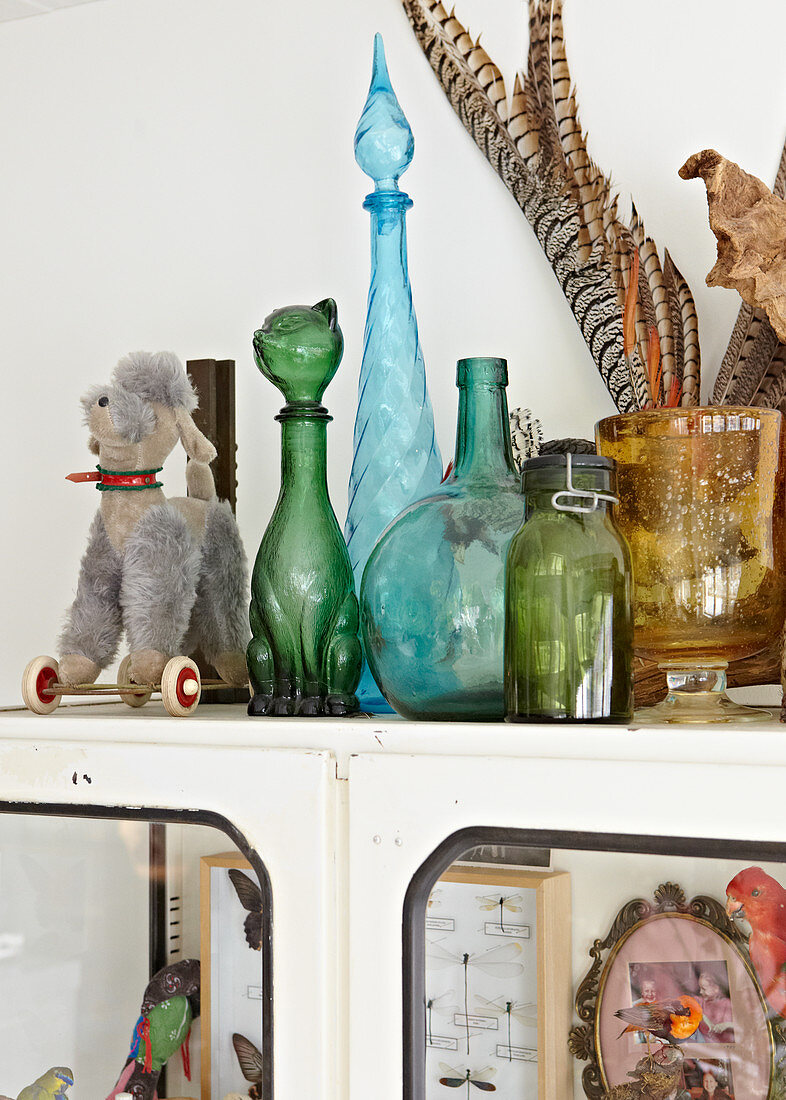 Decorative bottles of different colours and toys on top of vintage cabinet