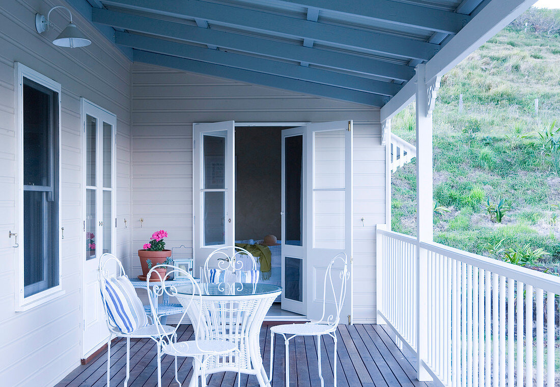 Table with decorative white metal chairs on the veranda of a wooden home