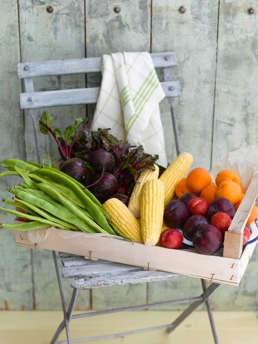 A crate of vegetables, sweet corn and fruit on a garden chair
