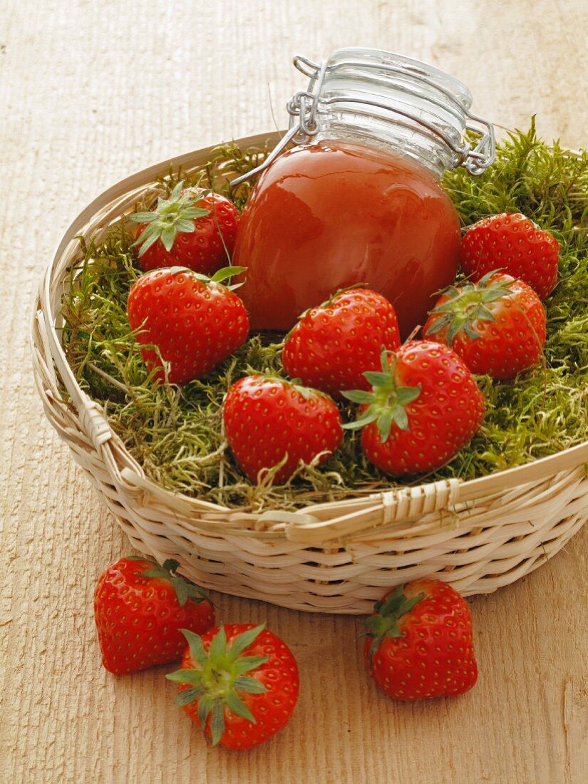 Erdbeermarmelade und frische Erdbeeren auf Moos im Korb