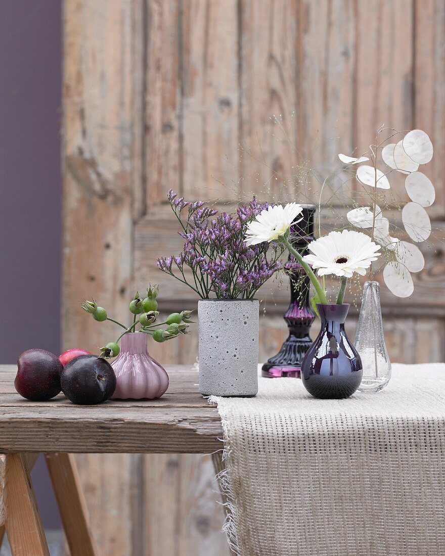 Flower vases and plums on a wooden table