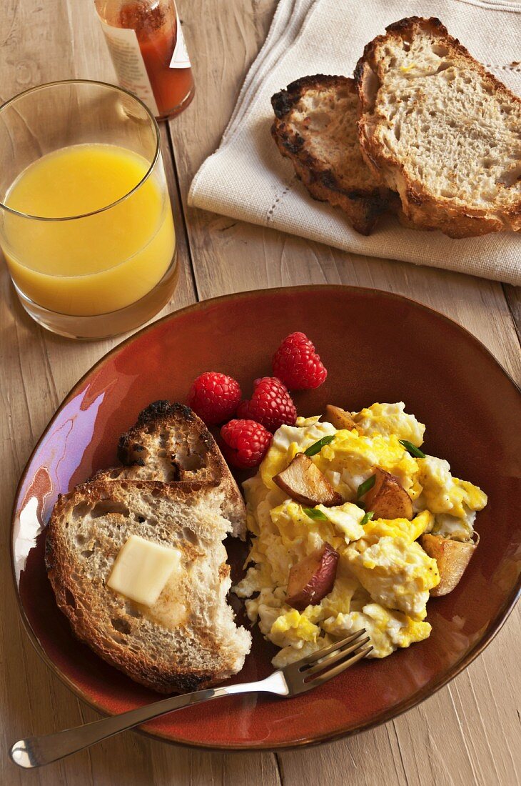 Frühstück mit Kartoffel-Rührei, Toastbrot, Butter und Orangensaft