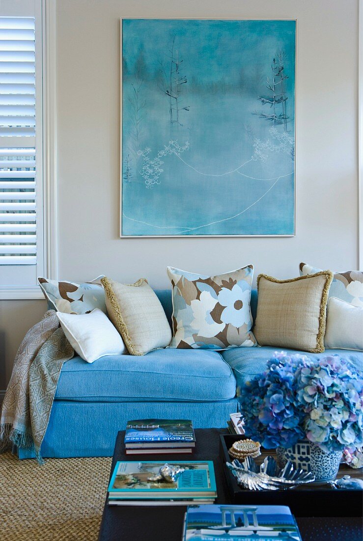 Türkisfarbene Couch unter Aquarellbild im selben Farbton; davor ein blauer Hortensienstrauss auf dem Couchtisch