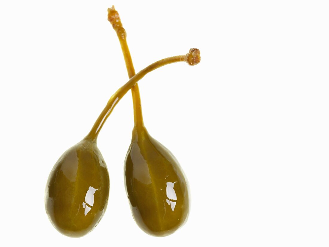 Two pickled capers against a white background