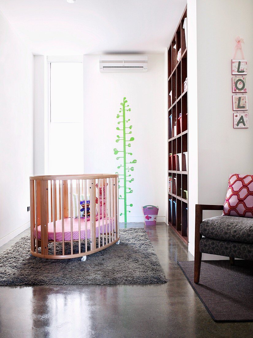 Bright, airy nursery with cot on soft woollen rug and cheerful green tree painted on wall