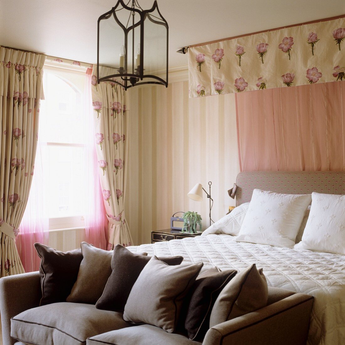 Scatter cushions on sofa at foot of double bed with canopy in traditional bedroom
