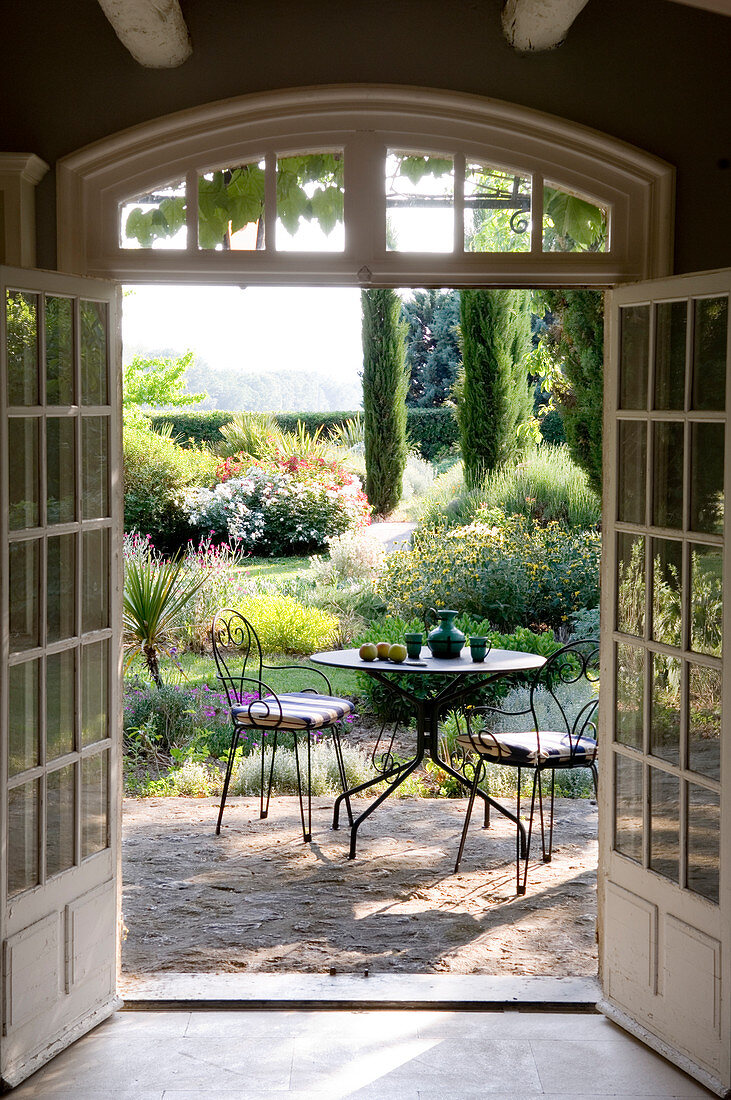 View of table and chairs in French garden through open terrace doors