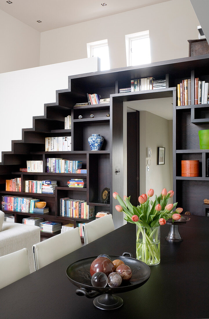 Custom-made staircase with integrated shelving leading to gallery; ornaments on Molteni dining table in foreground