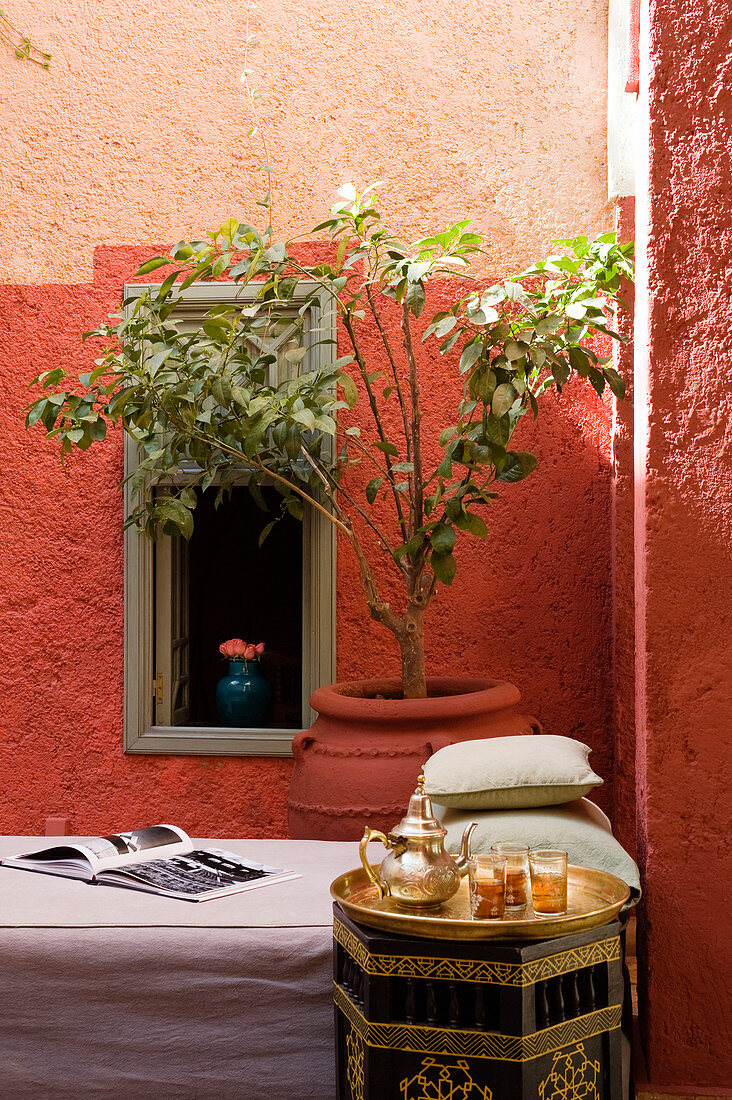 Orientalisches Teeservice aus Messing auf Beistelltisch neben Bett und Pflanzentopf in Ecke einer Loggia