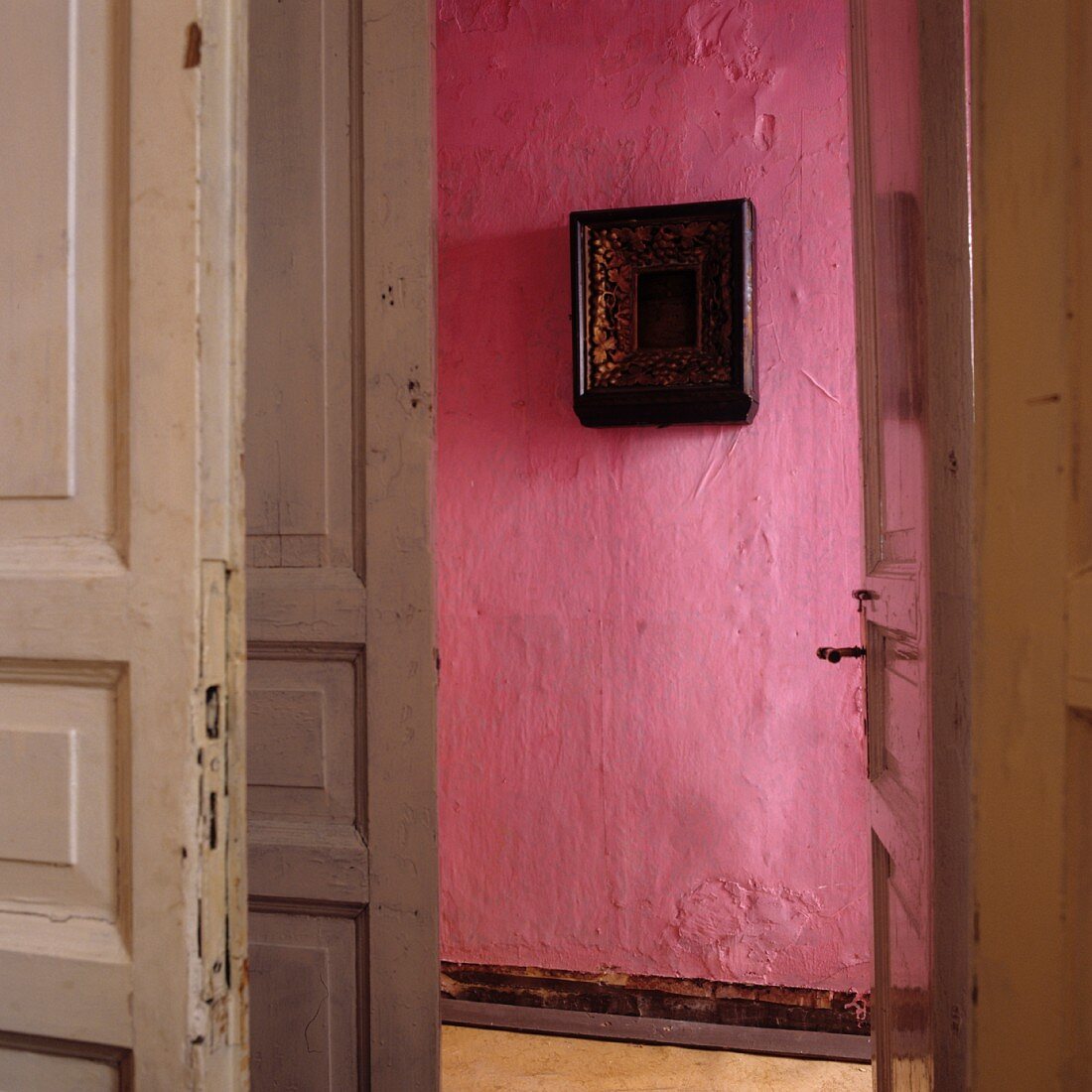 Blick durch offene Tür auf pinkfarbene Wand mit Bild im Flur einer Altbauwohnung