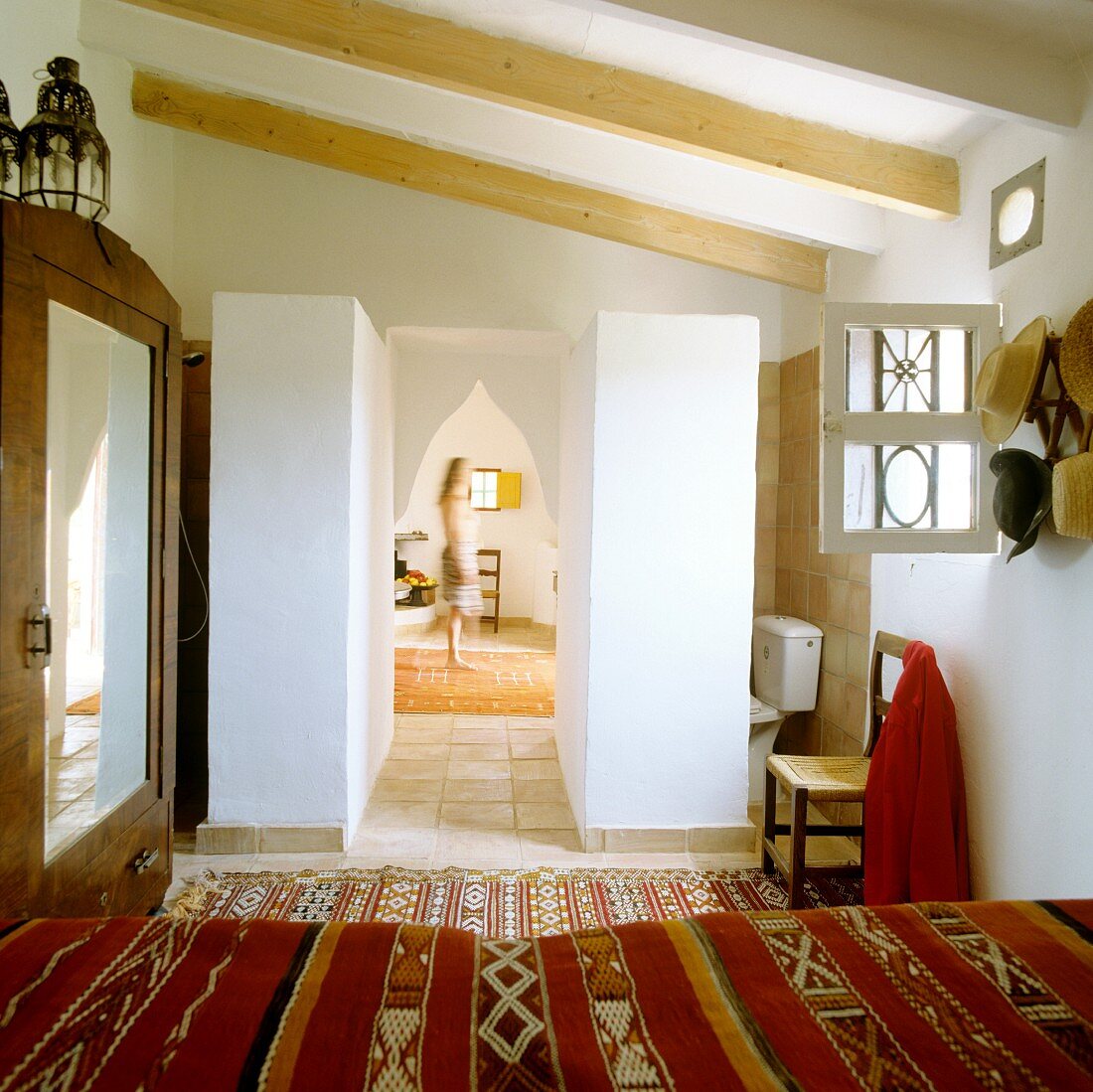 View across bed with ethnic bedspread to Oriental pointed archway and woman in hall