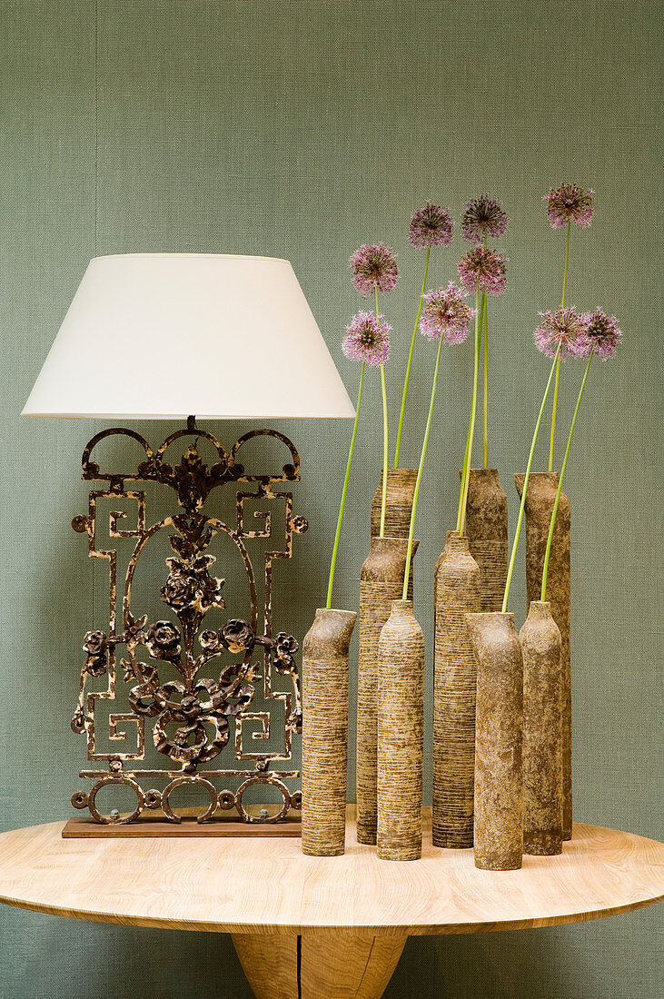 Tonvasengruppe mit einzelnen Blumen und Tischlampe mit weißem Schirm auf Vintage Metallfuss auf modernem Tisch vor stoffbezogener Wand