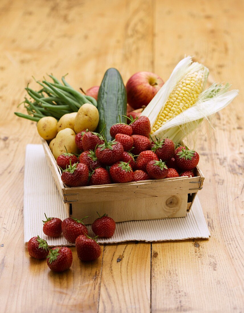 Strawberries, corn cobs, vegetables and apples in a wooden basket