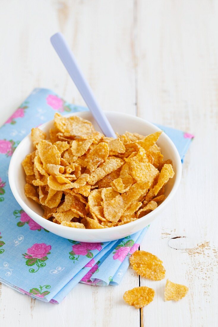 Cornflakes in Keramikschale mit Löffel auf bunter Serviette