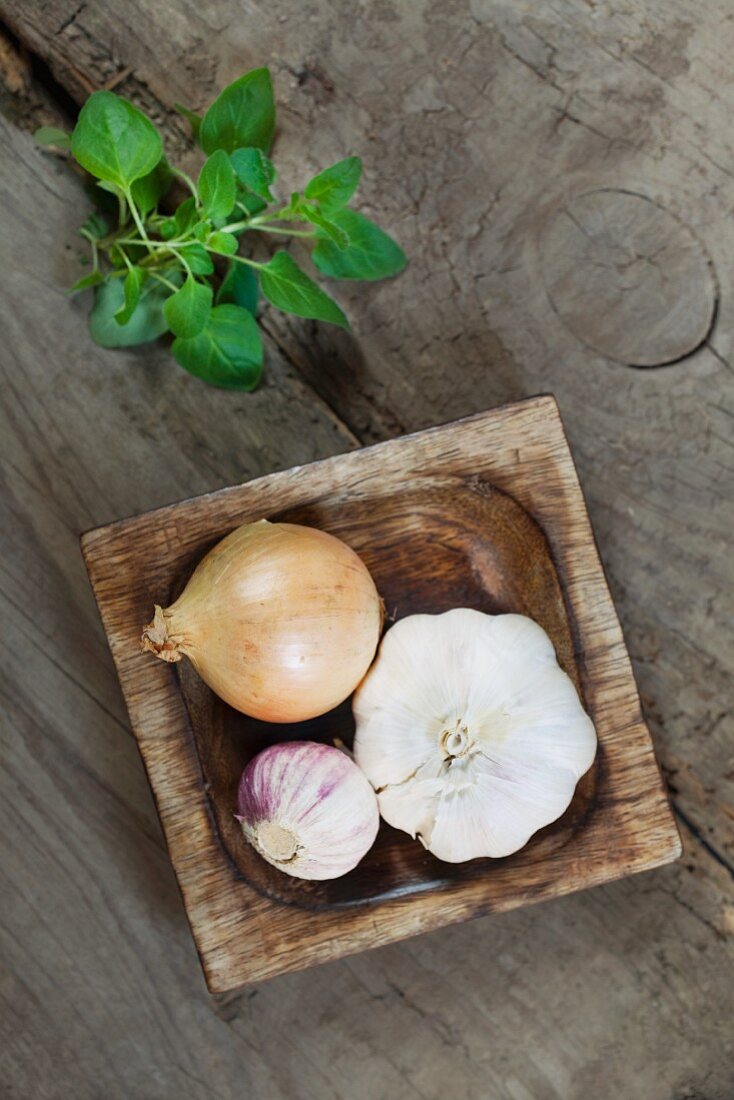 Zwiebel und Knoblauch in Holzschale, daneben Oregano