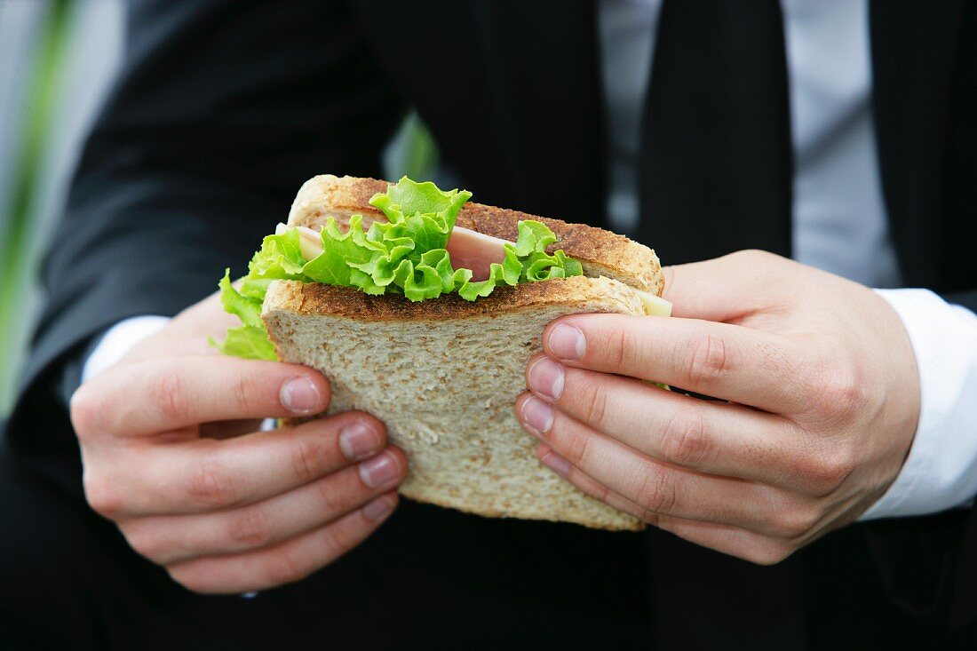 Mann hält ein Schinken-Käse-Sandwich
