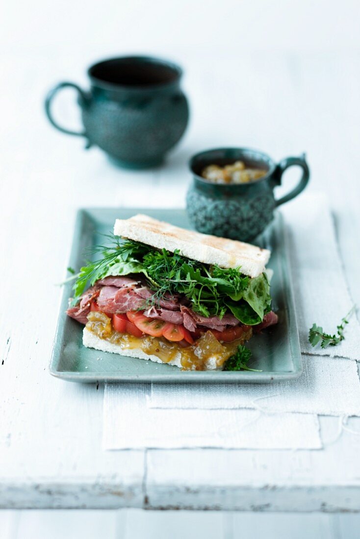Sandwich mit Tomatenrelish, Pastrami, Salatblättern und Kräutern