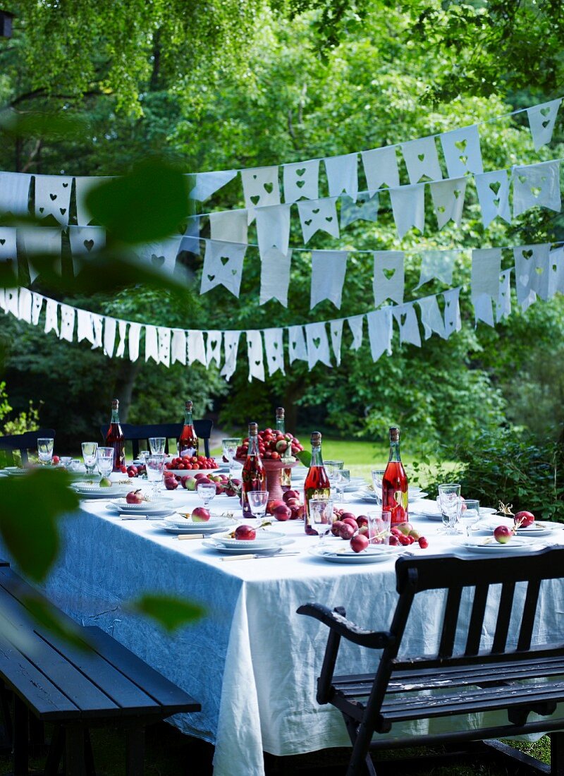 Festive set table below bunting strung between trees in garden