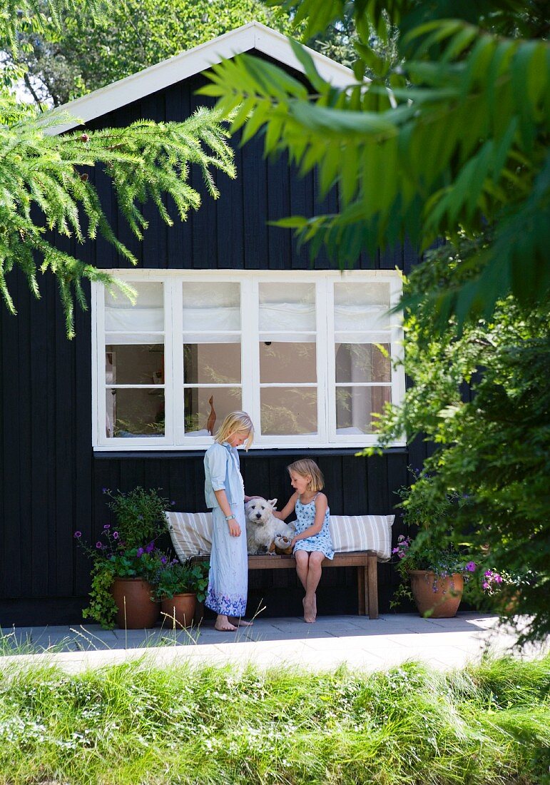 Children and dog on bench in front of wooden cottage