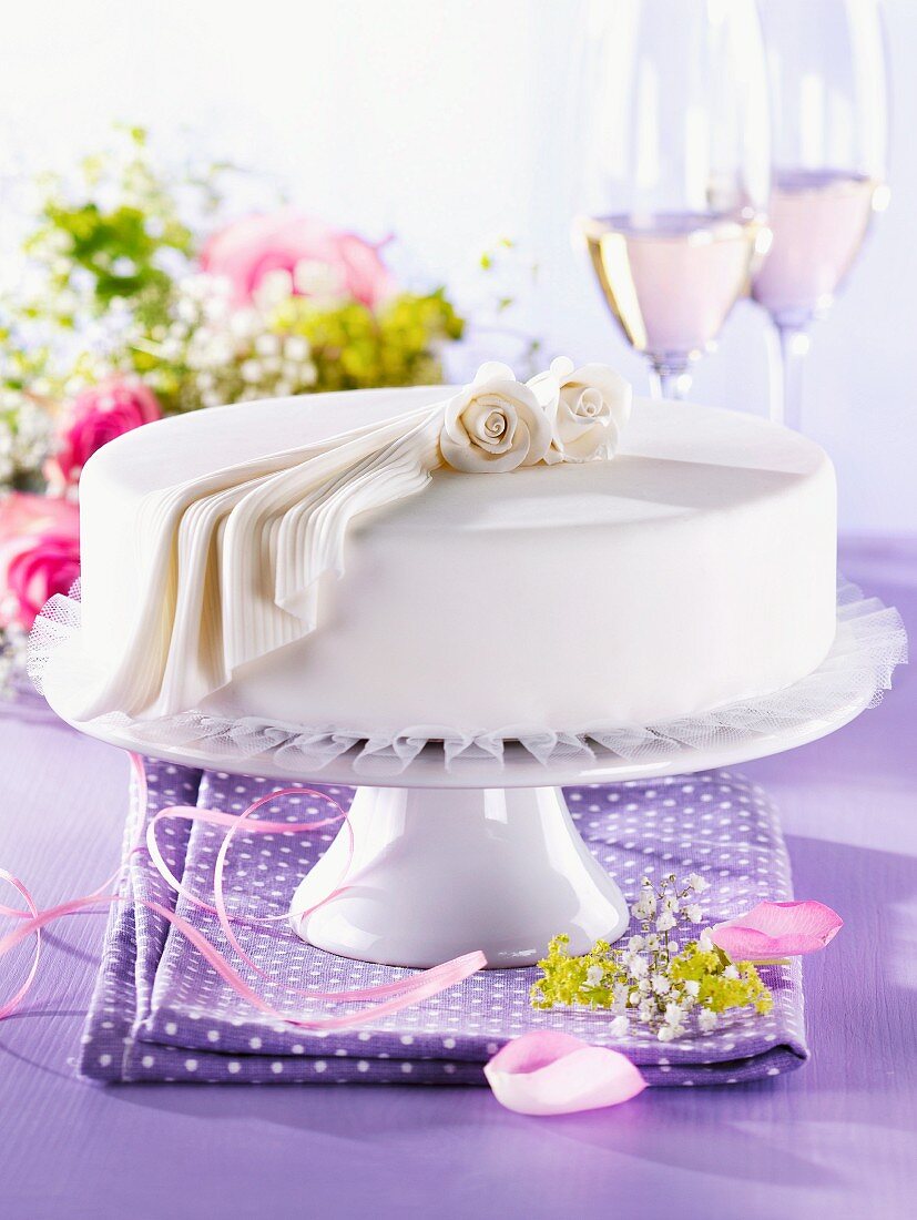 A white festive cake decorated with roses and fondant icing