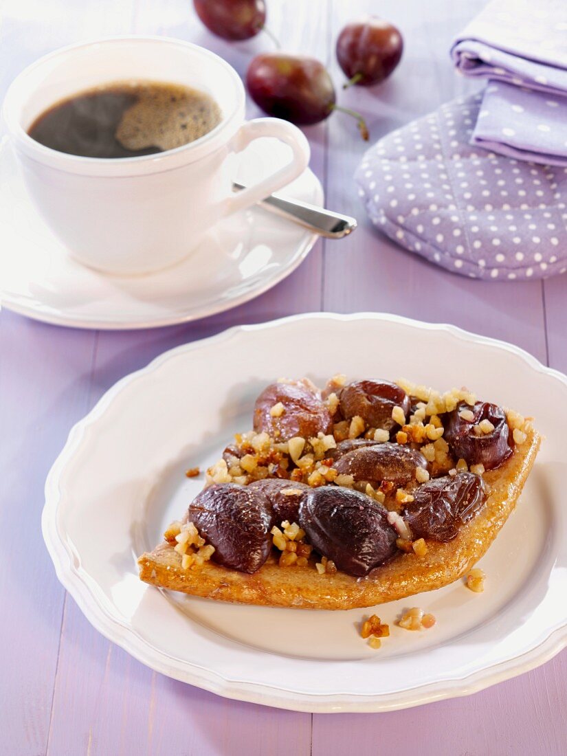 Damson cake with chopped almonds on a plate with a cup of coffee