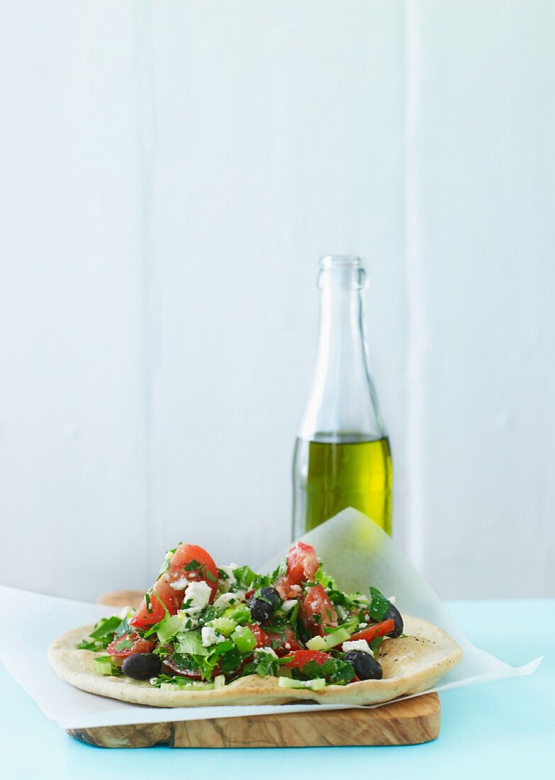 Griechischer Salat auf Fladenbrot vor Olivenölflasche