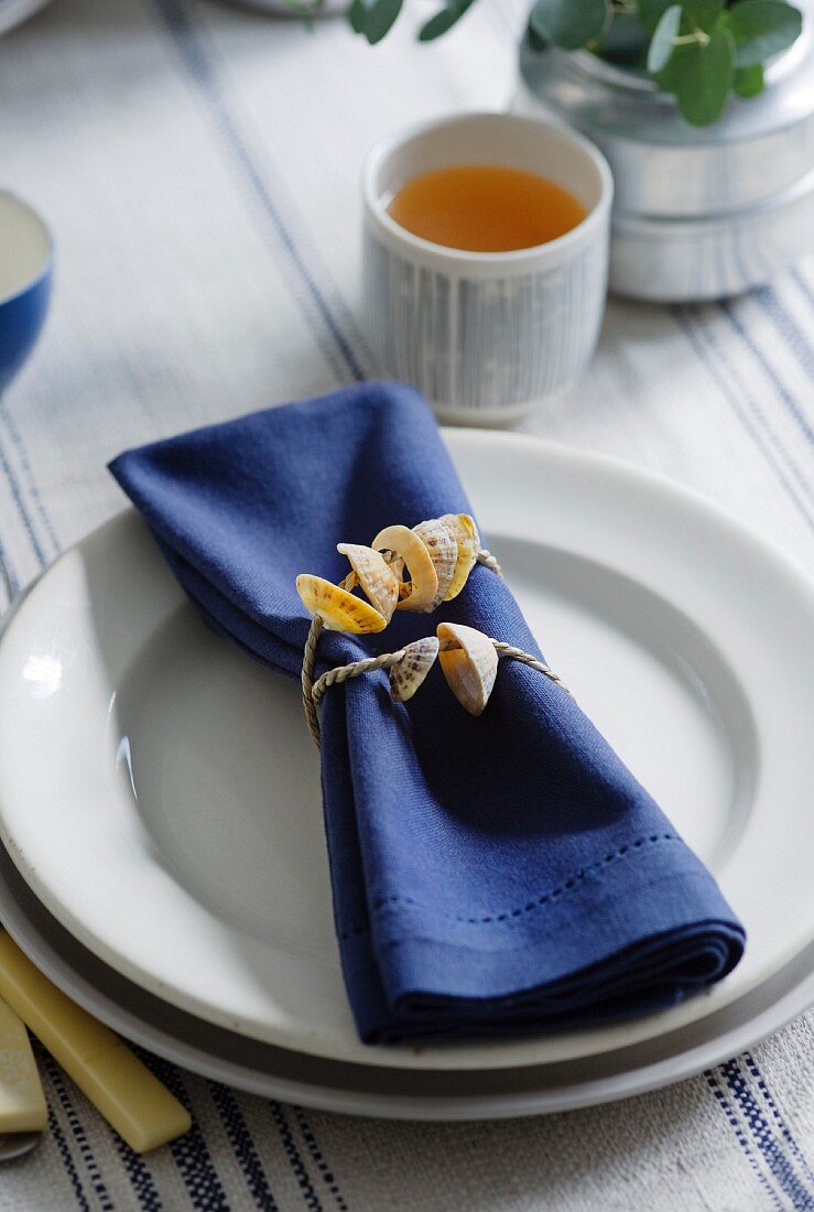A place setting with a blue napkin and a napkin ring made of shells
