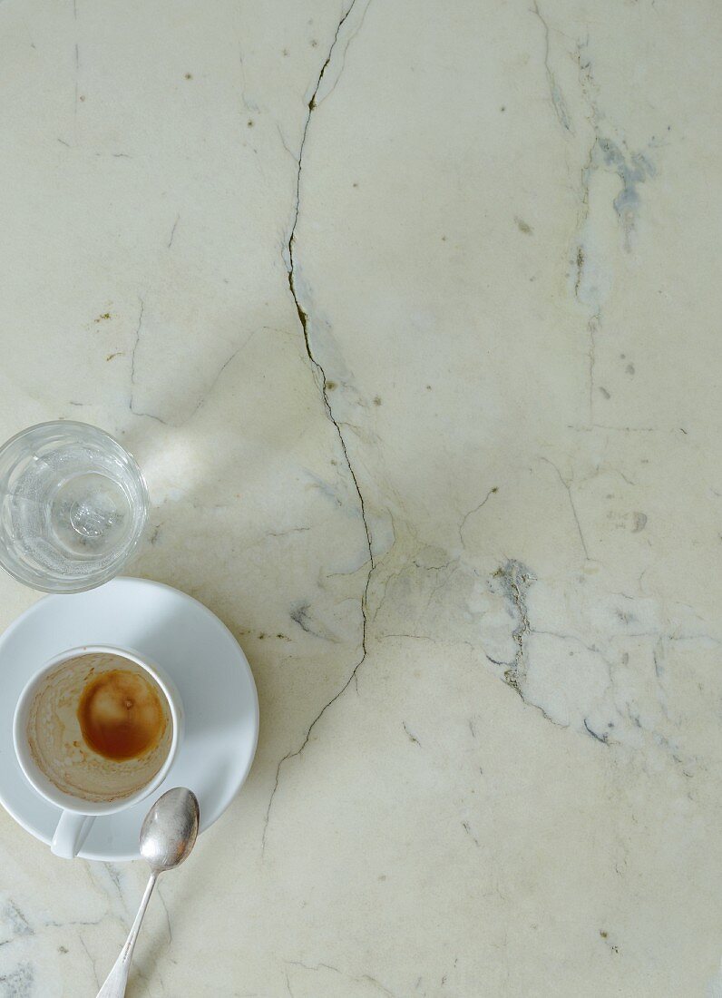 Ausgetrunkene Kaffeetasse und Wasserglas auf Marmortisch