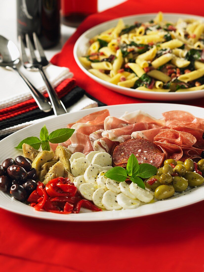 An anti-pasti platter and penne with pancetta and leafy vegetables (Italy)