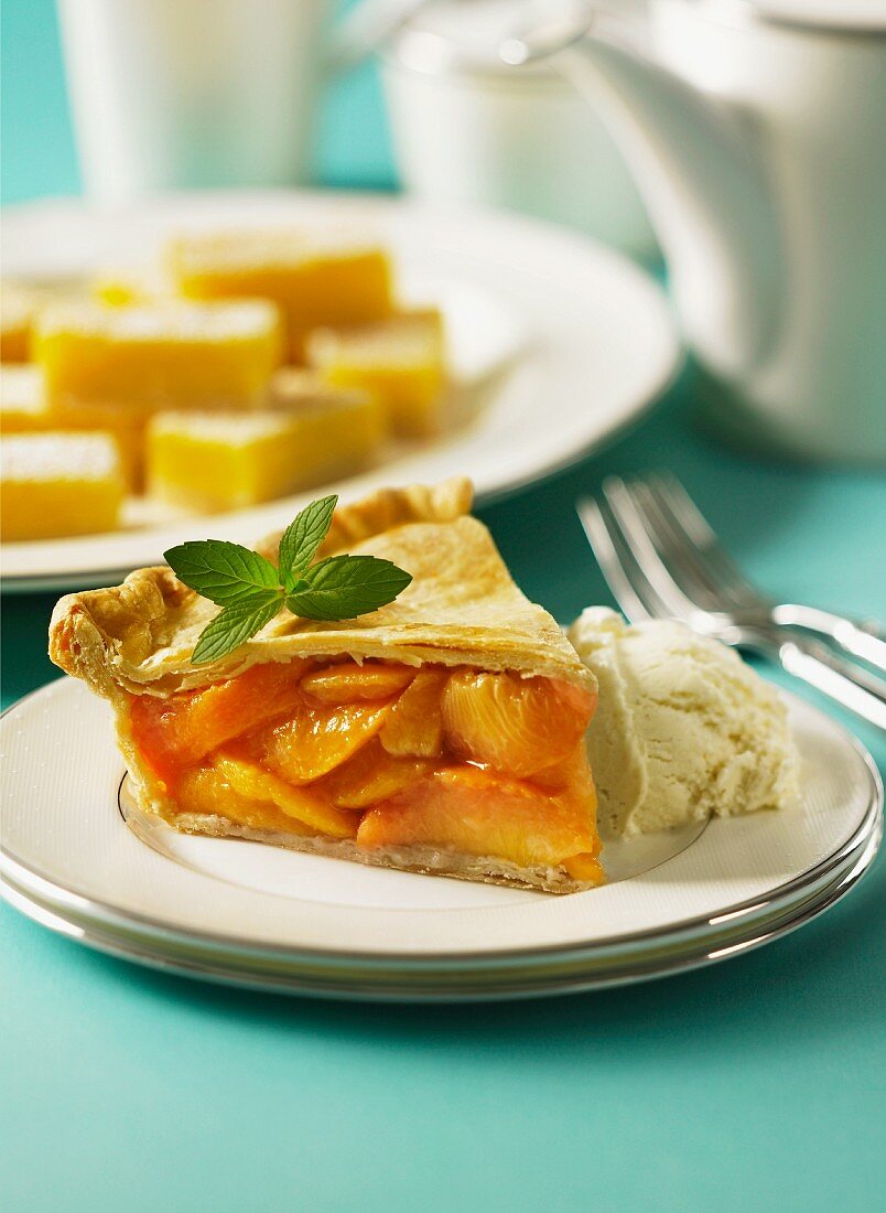 A slice of peach pie with vanilla ice cream and lemon wedges