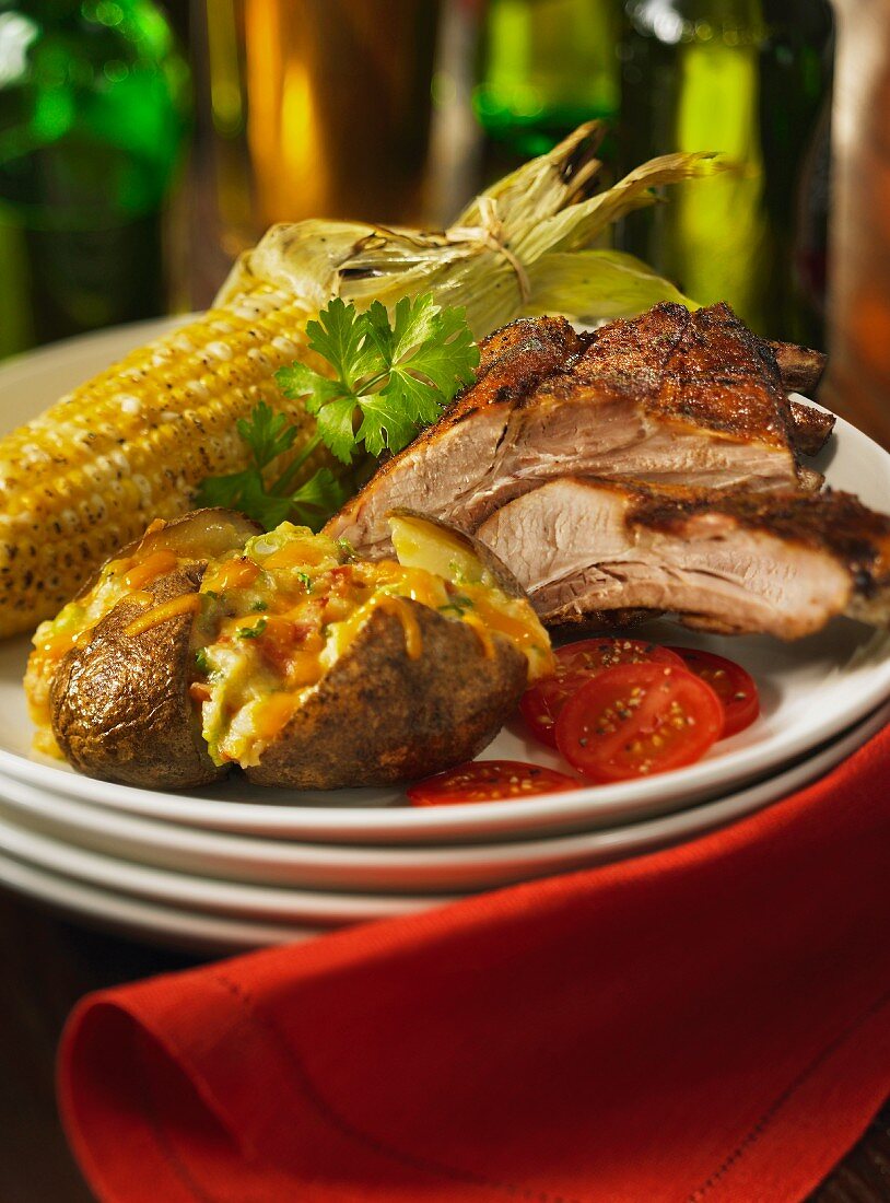 A grill platter with spare ribs, baked potatoes with Cheddar cheese and corn cobs