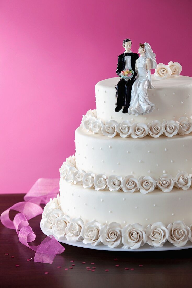A white, three tier wedding cake with decorative roses