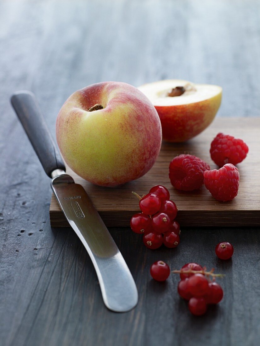 Peaches, redcurrants and raspberries on a wooden board with a knife