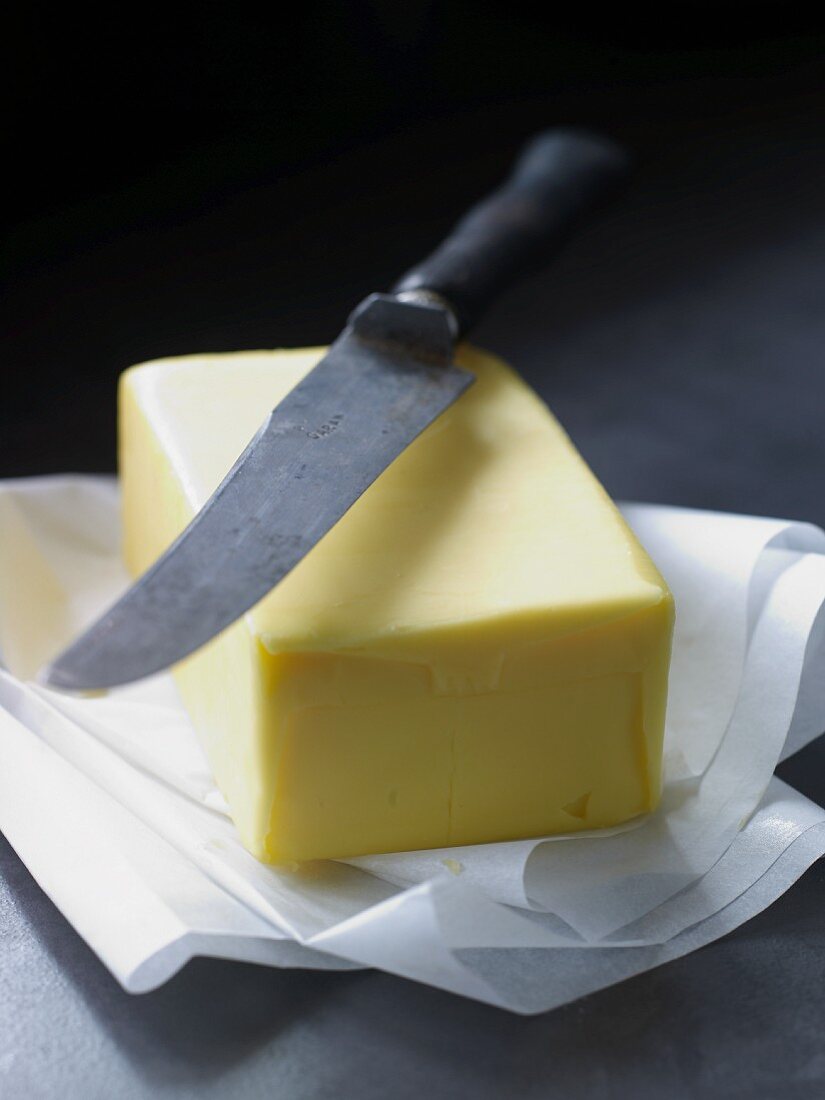 Ein Stück Butter auf Pergamentpapier mit Messer